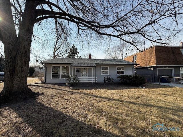 view of front of home featuring a chimney, roof with shingles, and a front yard