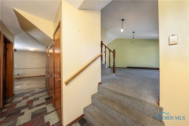 stairway featuring vaulted ceiling, a textured ceiling, and wainscoting