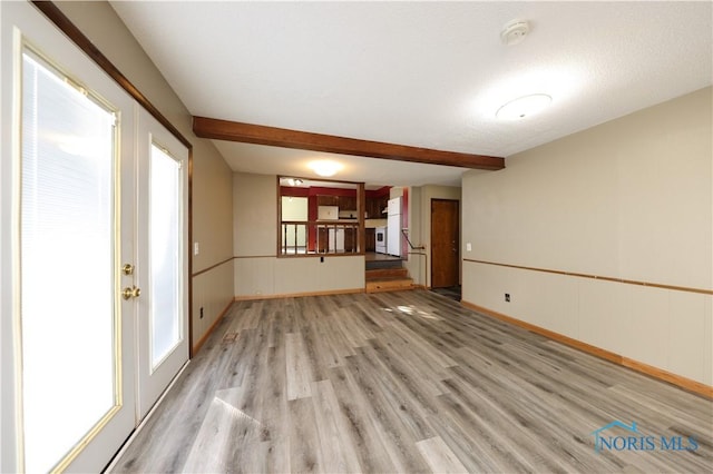 empty room with light wood-style floors, beamed ceiling, and baseboards