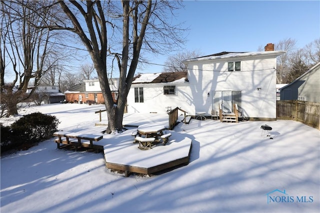 snow covered house with entry steps, fence, and a chimney