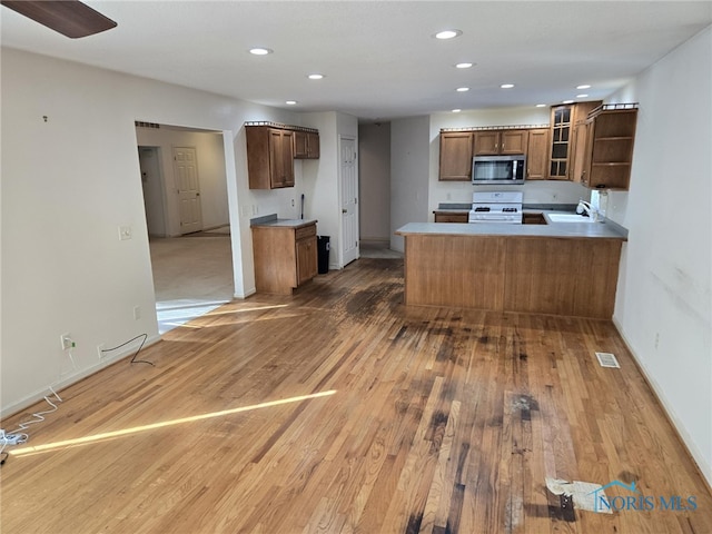 kitchen with white gas range oven, glass insert cabinets, stainless steel microwave, brown cabinets, and a peninsula