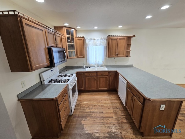 kitchen featuring a peninsula, white appliances, a sink, open shelves, and glass insert cabinets