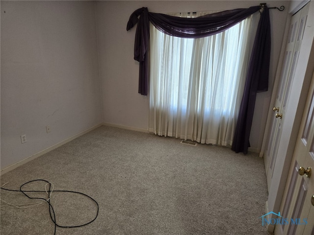 spare room featuring light carpet and baseboards