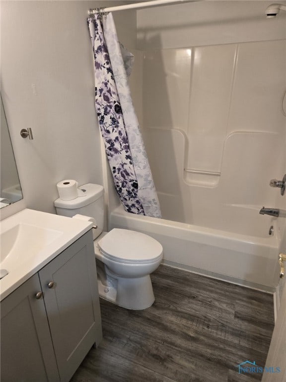 bathroom with toilet, wood finished floors, vanity, and shower / bathtub combination with curtain