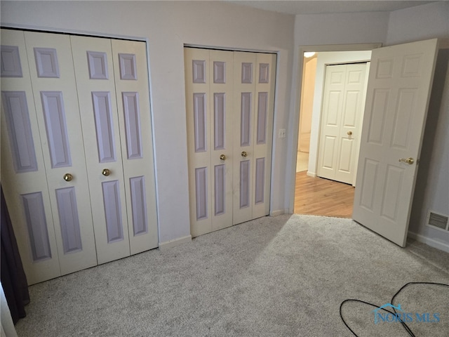 bedroom featuring light carpet, visible vents, and multiple closets