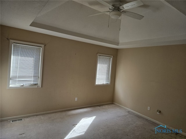 unfurnished room featuring a tray ceiling, light colored carpet, visible vents, ceiling fan, and baseboards