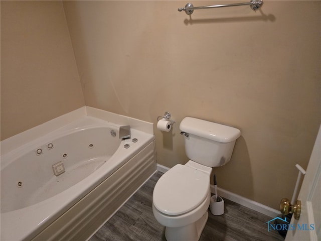 bathroom featuring wood finished floors, baseboards, toilet, and a tub with jets