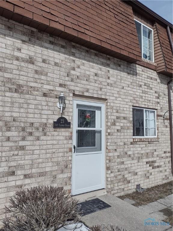 entrance to property with roof with shingles and brick siding