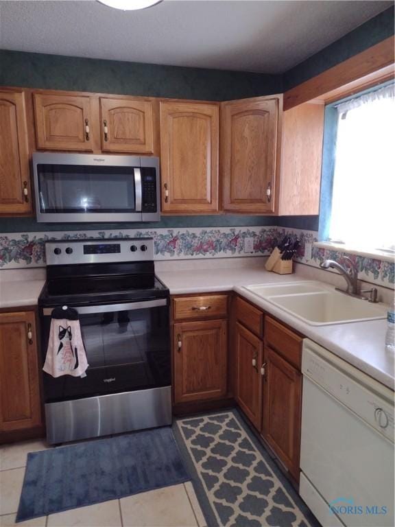 kitchen featuring brown cabinets, stainless steel appliances, a sink, and light countertops