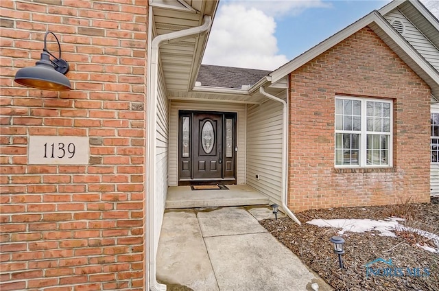 doorway to property featuring brick siding and roof with shingles