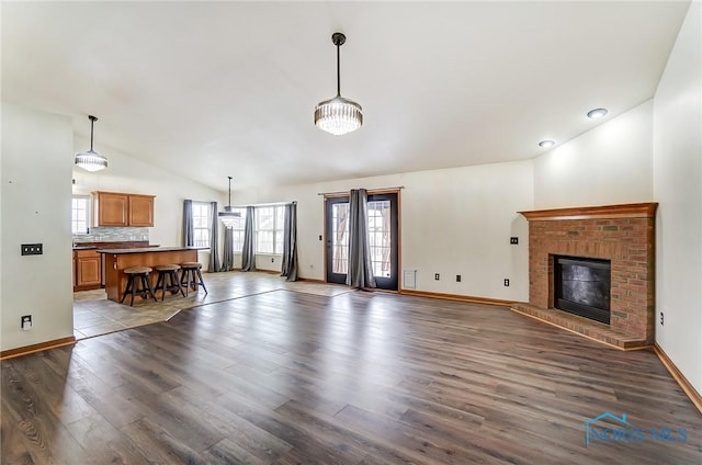 unfurnished living room with high vaulted ceiling, dark wood-style flooring, a brick fireplace, and baseboards