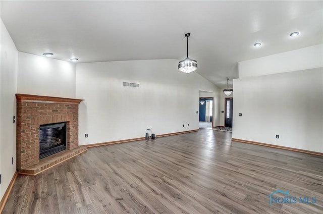 unfurnished living room with a fireplace, visible vents, vaulted ceiling, wood finished floors, and baseboards