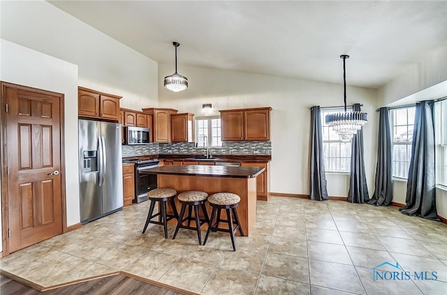 kitchen with stainless steel appliances, a kitchen island, brown cabinets, dark countertops, and pendant lighting