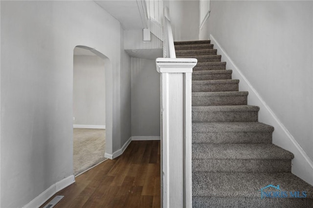 stairway featuring arched walkways, visible vents, baseboards, and wood finished floors