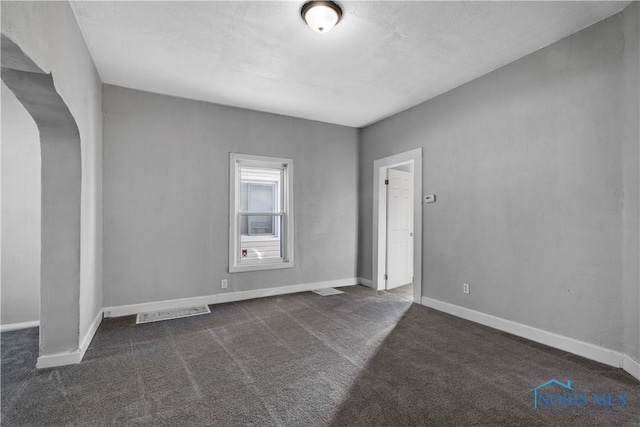 spare room with visible vents, baseboards, and dark colored carpet