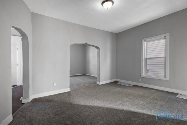 unfurnished room with visible vents, arched walkways, dark colored carpet, and baseboards