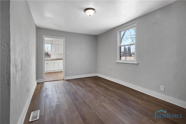 empty room featuring baseboards, visible vents, and dark wood-type flooring