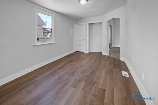 unfurnished bedroom featuring dark wood-style floors, arched walkways, visible vents, and baseboards