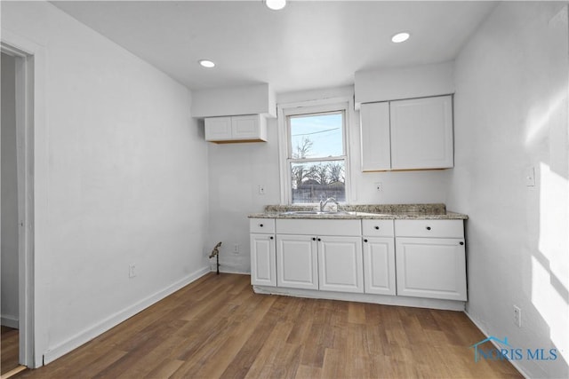 kitchen featuring light wood-type flooring, baseboards, white cabinetry, and a sink