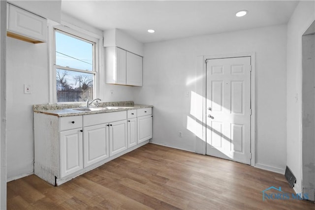 kitchen with light countertops, light wood-type flooring, a sink, and white cabinets