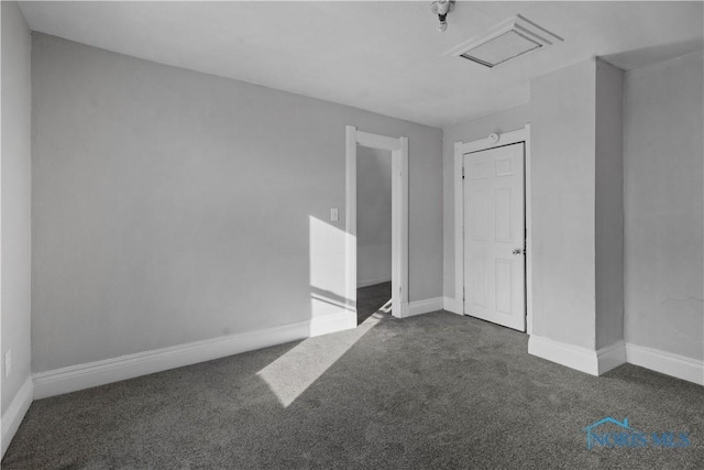 unfurnished room with attic access, visible vents, dark carpet, and baseboards