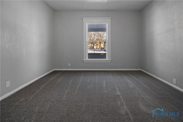 unfurnished room featuring dark carpet and baseboards