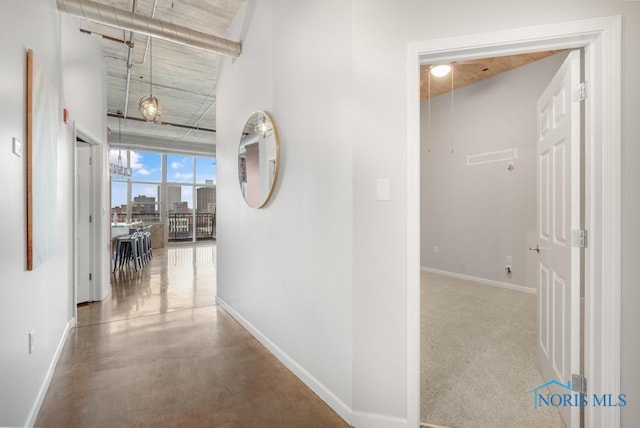 corridor with finished concrete flooring, attic access, a view of city, and baseboards