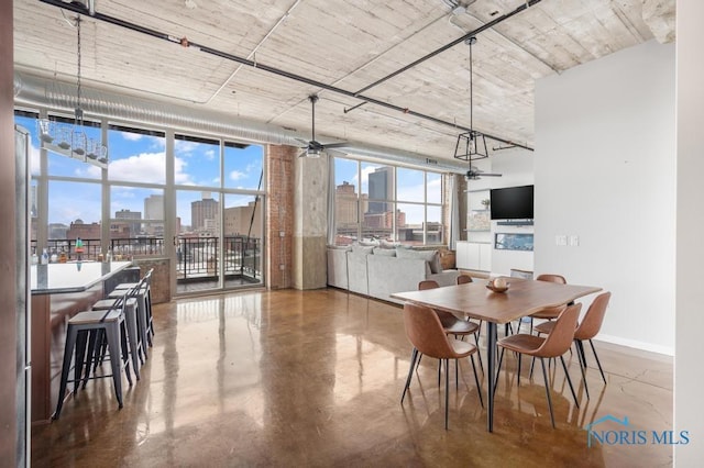 dining room featuring baseboards, a ceiling fan, finished concrete floors, a city view, and floor to ceiling windows