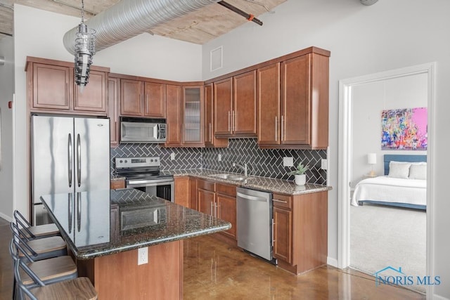 kitchen with decorative backsplash, dark stone counters, appliances with stainless steel finishes, brown cabinets, and a sink