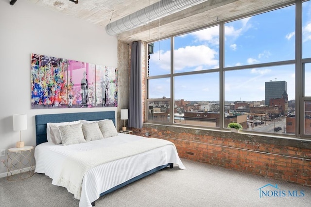 carpeted bedroom with a view of city and brick wall