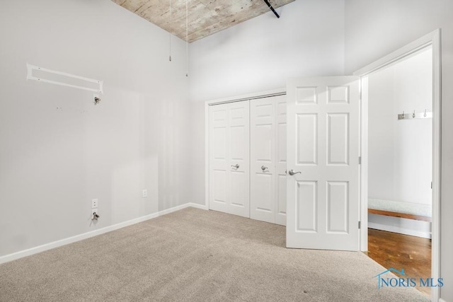 unfurnished bedroom with a high ceiling, a closet, carpet flooring, and baseboards