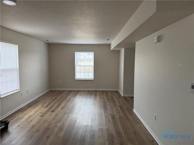 spare room with dark wood finished floors, a textured ceiling, and baseboards