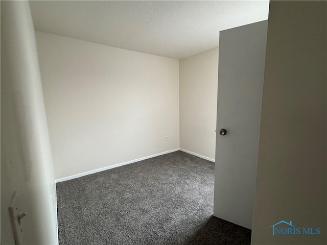 spare room featuring dark colored carpet and baseboards