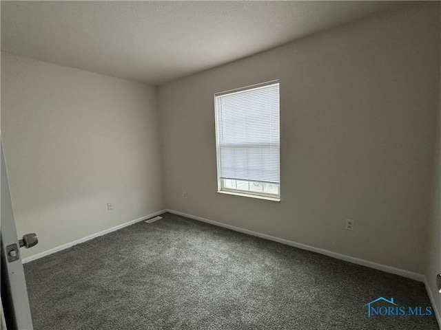 empty room featuring dark colored carpet, visible vents, and baseboards