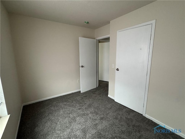 unfurnished bedroom with dark carpet and baseboards