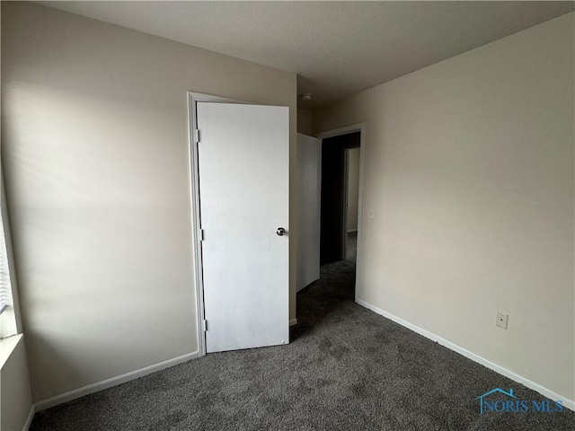 unfurnished bedroom featuring dark carpet and baseboards