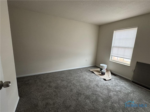 unfurnished room featuring a textured ceiling, dark carpet, and baseboards