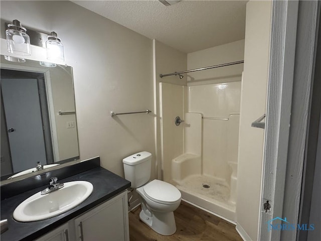 bathroom featuring toilet, a shower stall, a textured ceiling, wood finished floors, and vanity