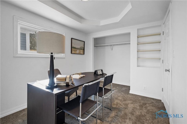 office area with baseboards, dark colored carpet, and a raised ceiling