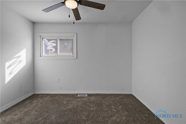 spare room featuring dark colored carpet, visible vents, ceiling fan, and baseboards