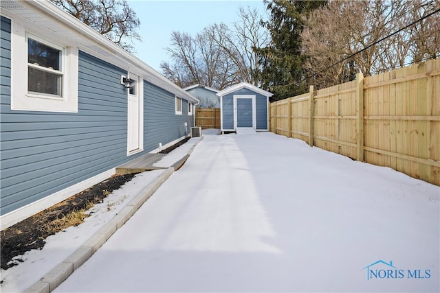 yard layered in snow featuring a fenced backyard, an outdoor structure, and a storage shed