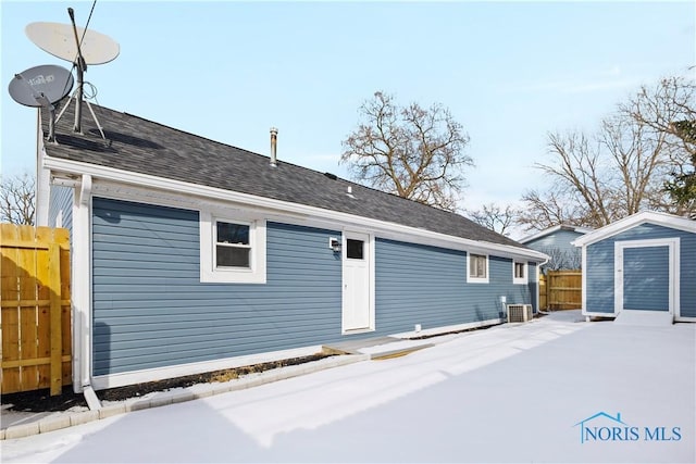 rear view of house with central air condition unit, a shingled roof, fence, and an outbuilding