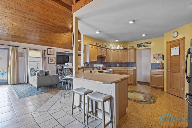 kitchen with white range with electric stovetop, a peninsula, light countertops, a kitchen bar, and backsplash