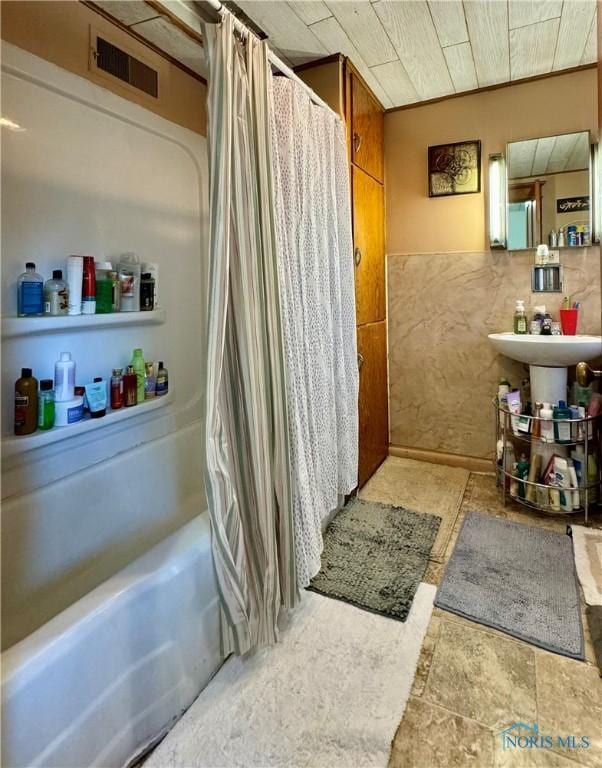 full bathroom with tile walls, stone finish flooring, visible vents, and shower / tub combo with curtain