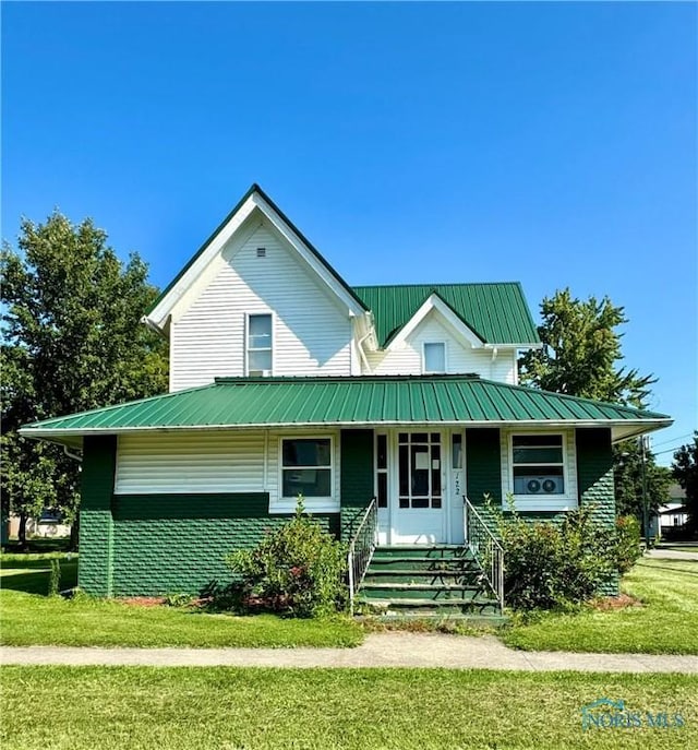 view of front facade featuring brick siding, metal roof, and a front yard