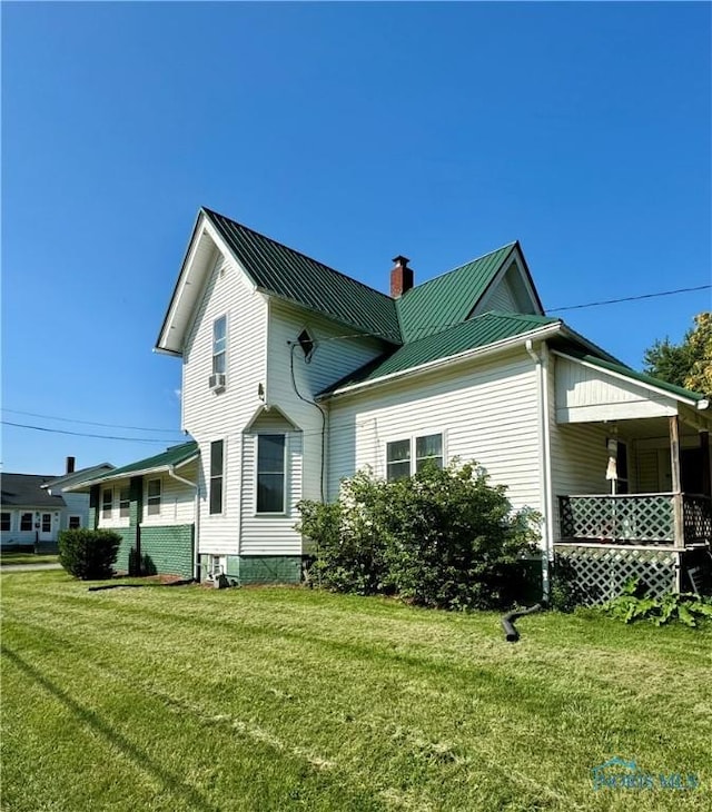 back of property featuring a chimney, metal roof, and a lawn