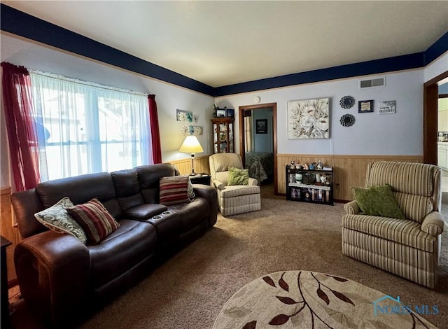 carpeted living area featuring wainscoting, visible vents, and wood walls