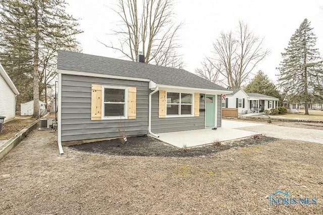 bungalow-style home featuring a patio, roof with shingles, and central air condition unit