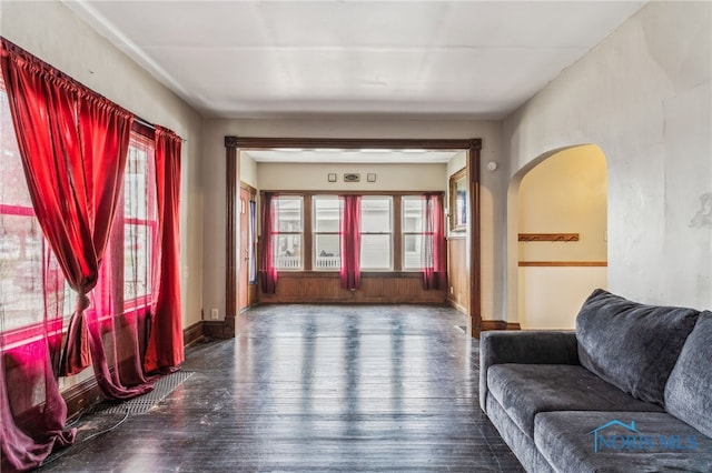 living room featuring baseboards, arched walkways, and dark wood-style flooring