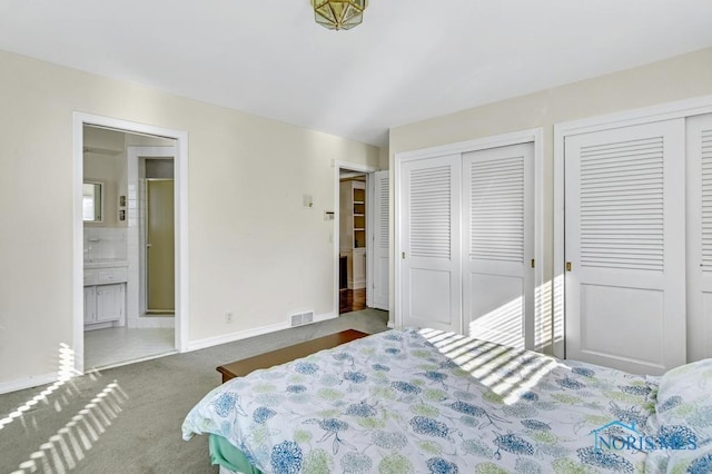 bedroom featuring visible vents, baseboards, multiple closets, dark colored carpet, and ensuite bath